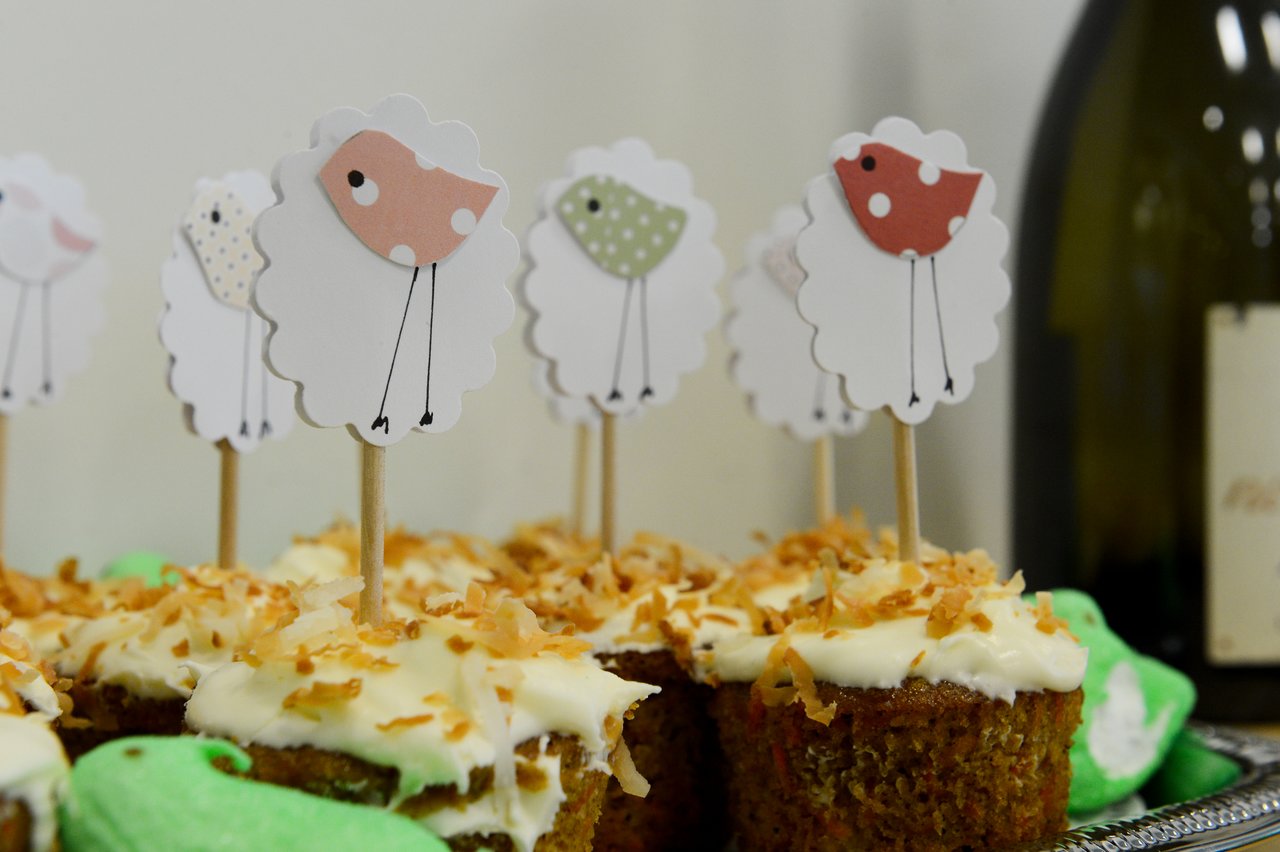 Cupcakes with white frosting and toasted coconut, decorated with sheep-shaped toppers on sticks at a baby shower.