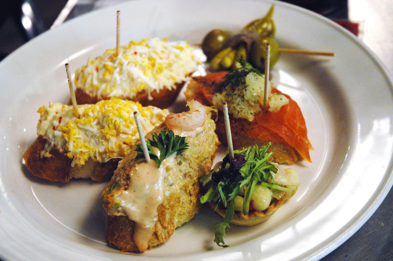 A plate of assorted tapas with seafood, vegetables, and creamy toppings, each secured with a toothpick.
