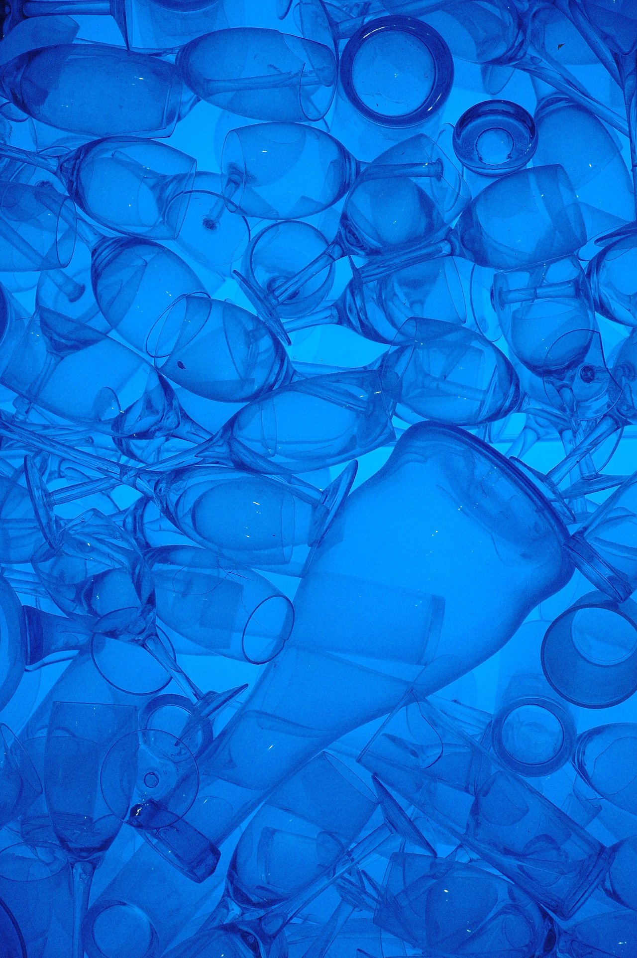 A collection of transparent glass cups and wine glasses stacked together, illuminated by a blue light.