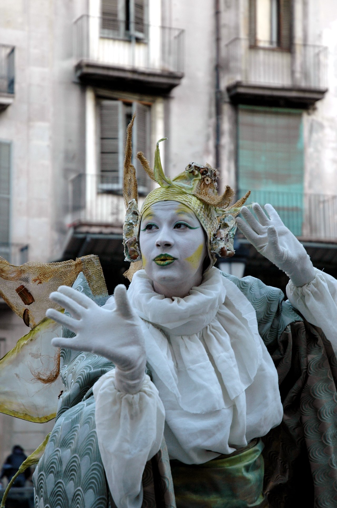 A street performer in an elaborate costume and white face paint poses with expressive hand gestures on Las Ramblas.