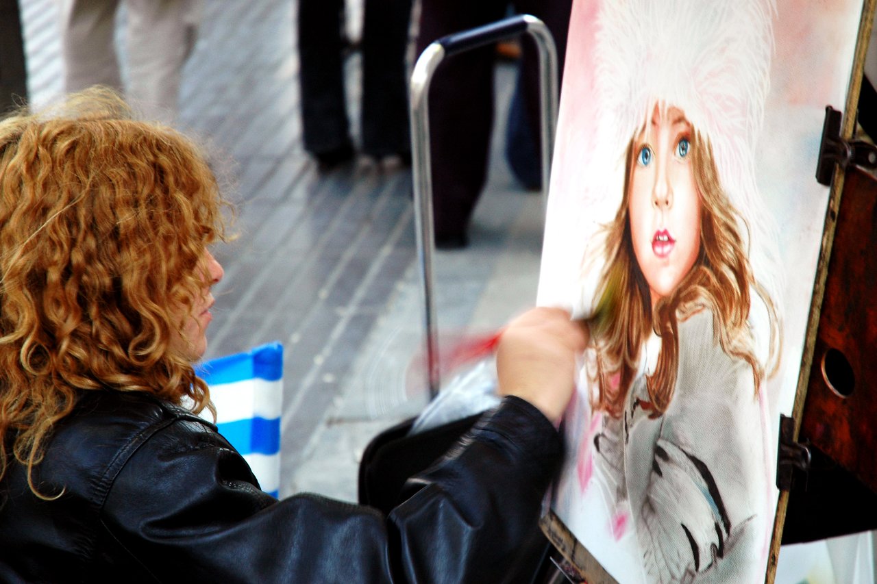 An artist paints a detailed portrait of a young girl wearing a fluffy hat on a busy street.