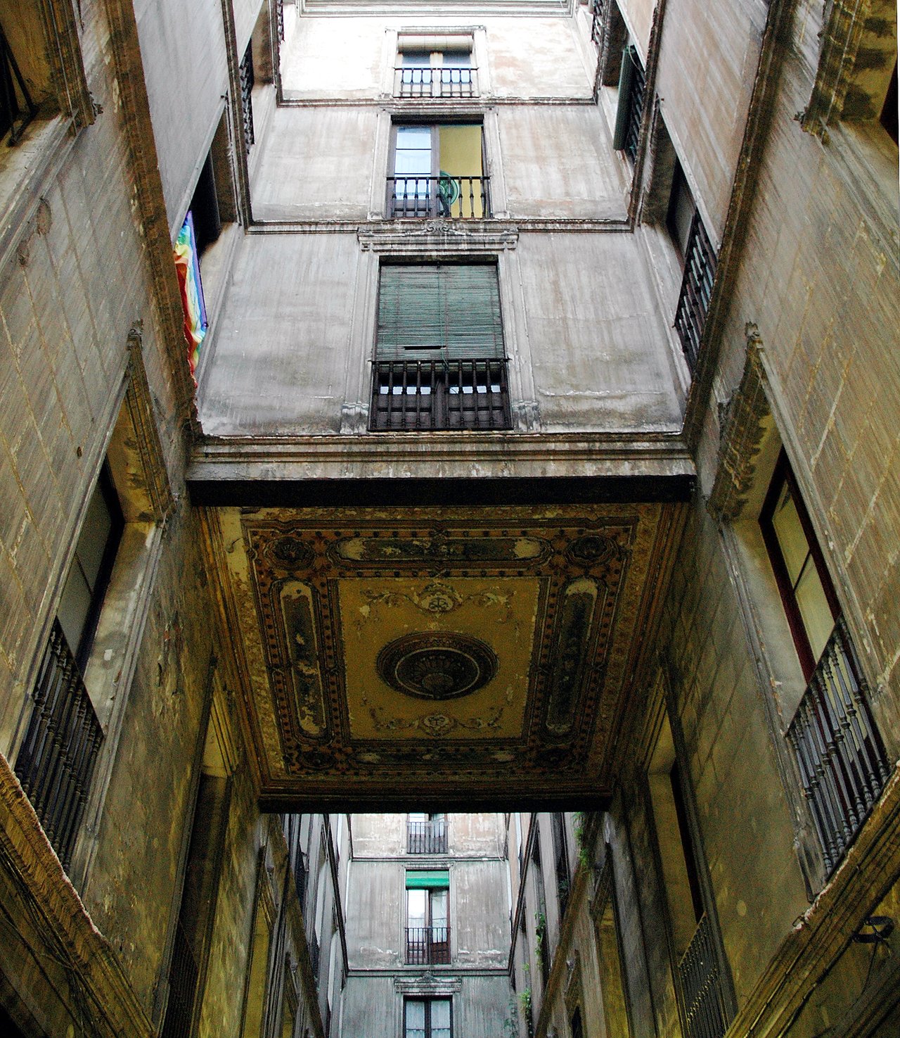 Narrow street in Barcelona's old city, surrounded by tall, aged buildings with balconies and a decorated overhead passage.