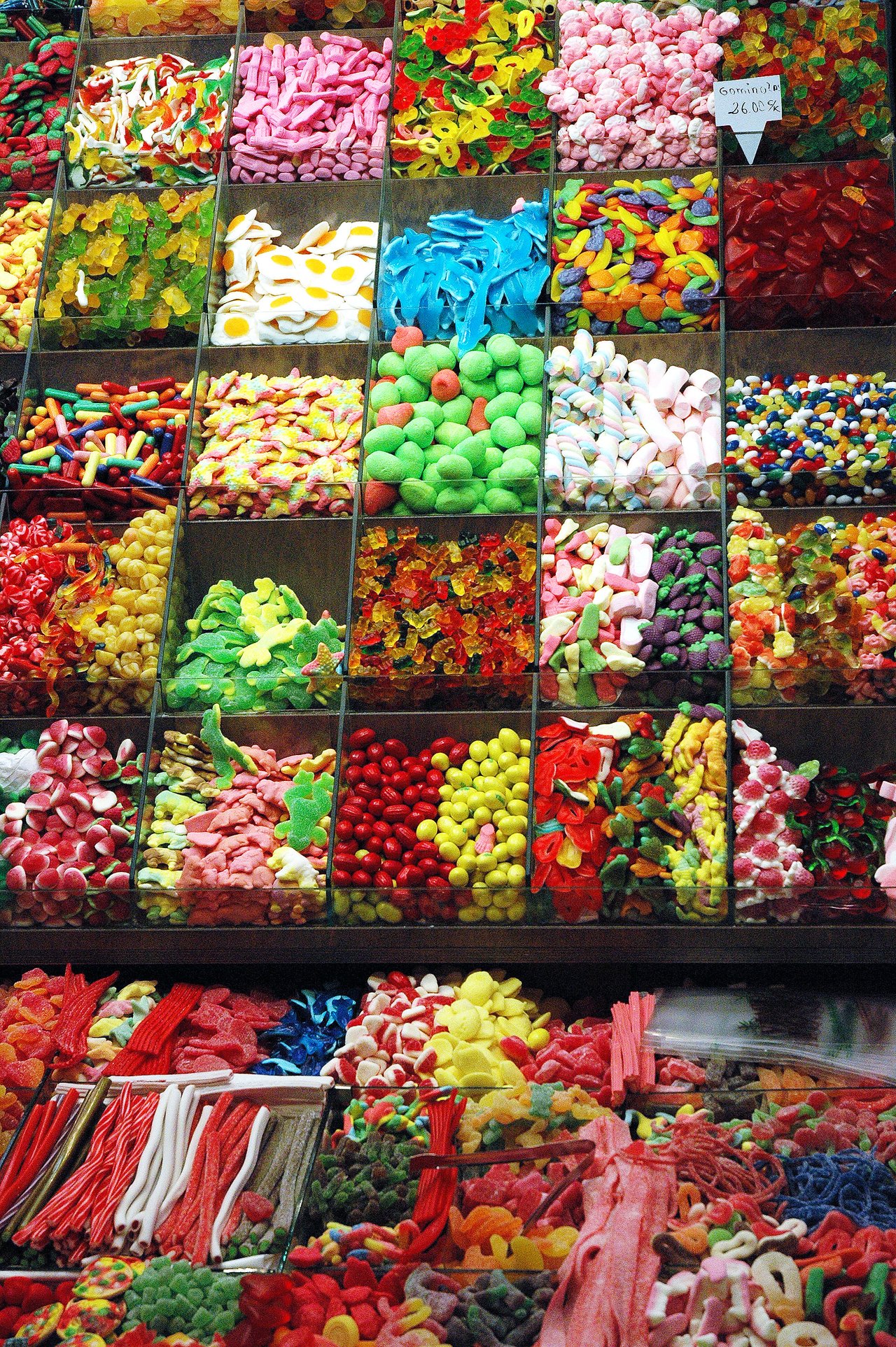 A market stall displaying a variety of colorful candies in clear bins, including gummies, licorice, and marshmallows.