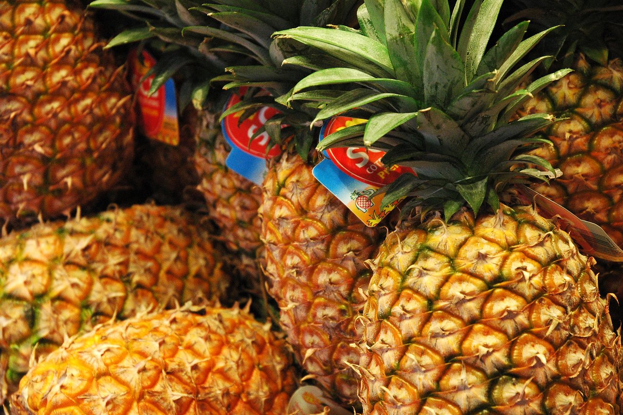 A pile of fresh pineapples with green leaves and price tags at a street market.