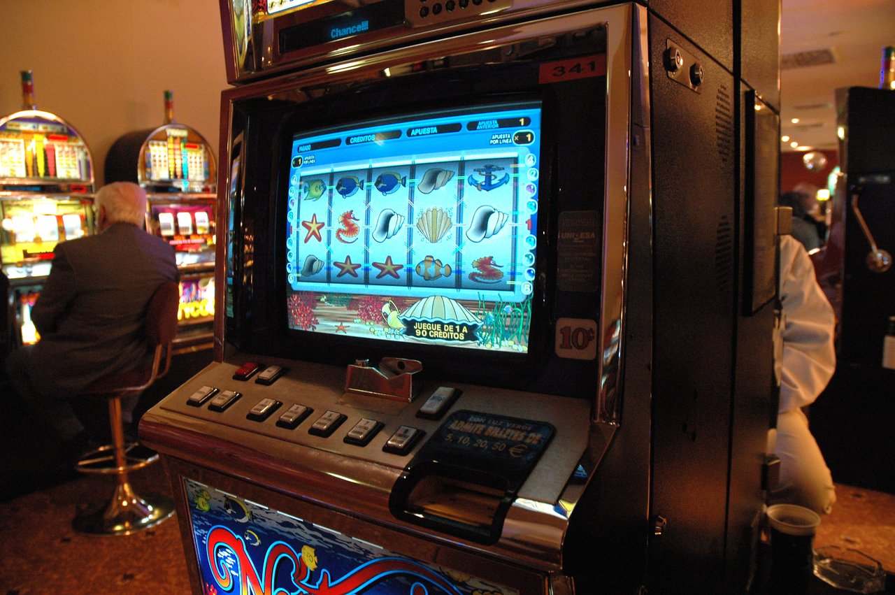 A slot machine with an ocean-themed display in a casino, with people playing nearby.
