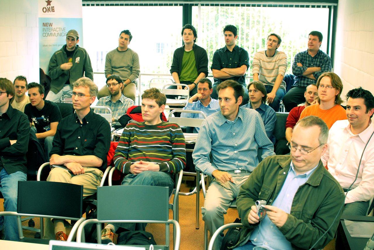 A group of people attentively listening at a Belgian Drupal User Group meeting, discussing Drupal modules and internationalization.