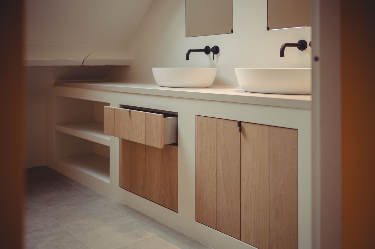 Bathroom cabinets in oak, one drawer slightly open, with white sinks and black faucets.