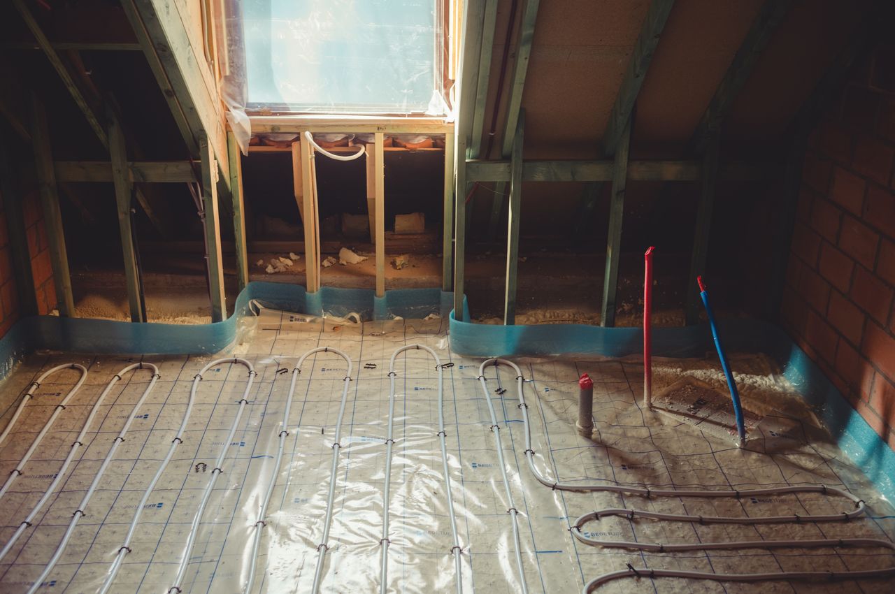 Underfloor heating pipes are being installed in the bathroom, with plumbing connections for the bathtub already in place.