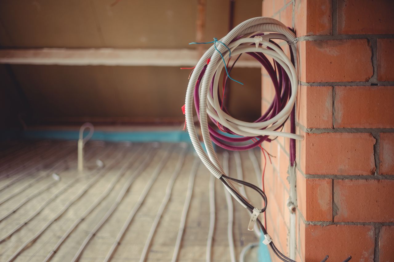 Coiled electrical and communication cables hang on a brick wall, with more cables laid out on the floor.