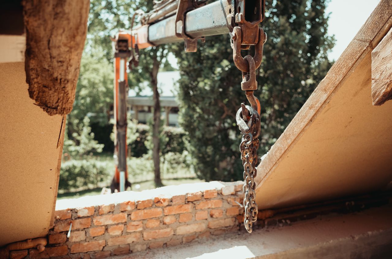 A crane lifts construction supplies through an opening in the roof of a building under renovation.