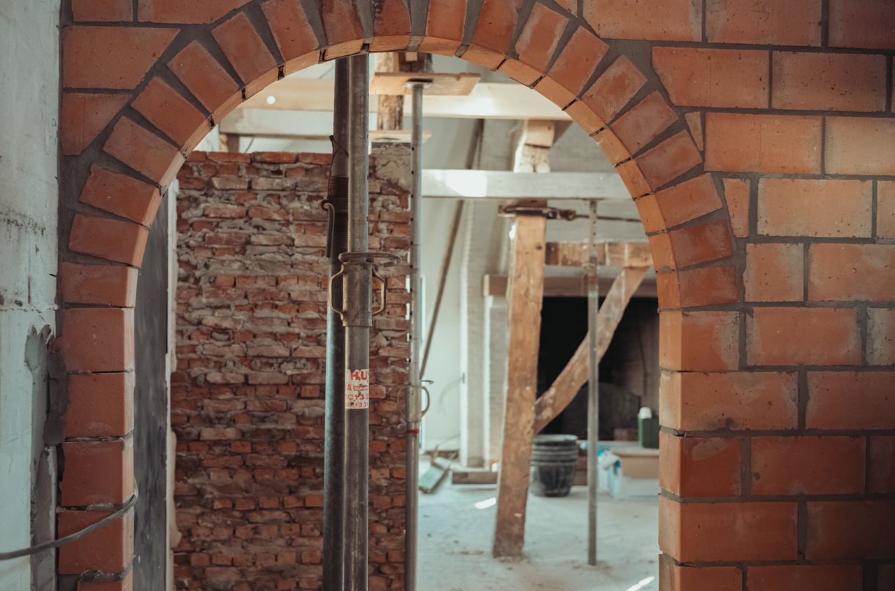 A brick archway under construction, with support beams and scaffolding in a partially renovated barn.