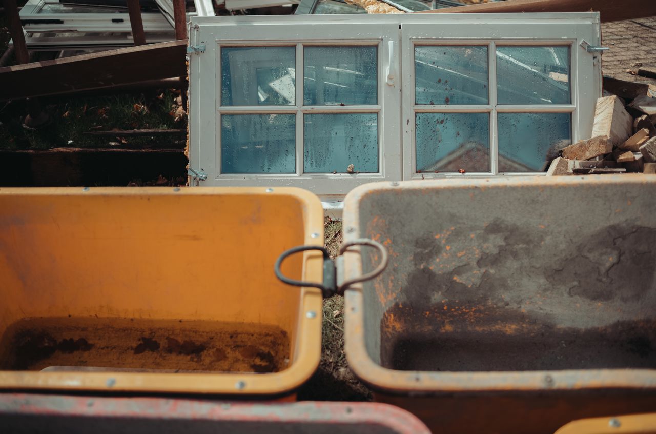 Piles of demolition waste, including old windows and wood, with empty wheelbarrows in the foreground.