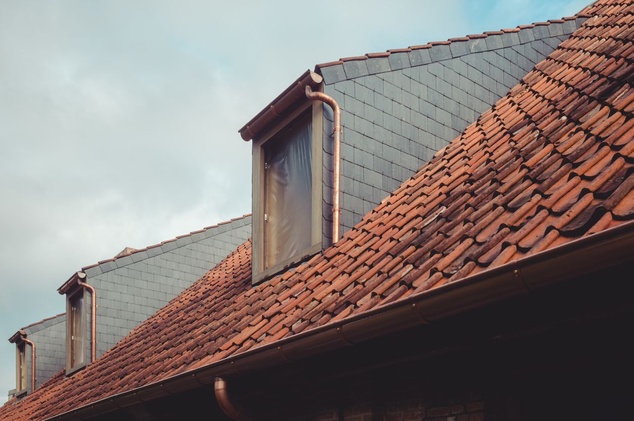 A roof with new dormer windows, gutters, and tiles installed.
