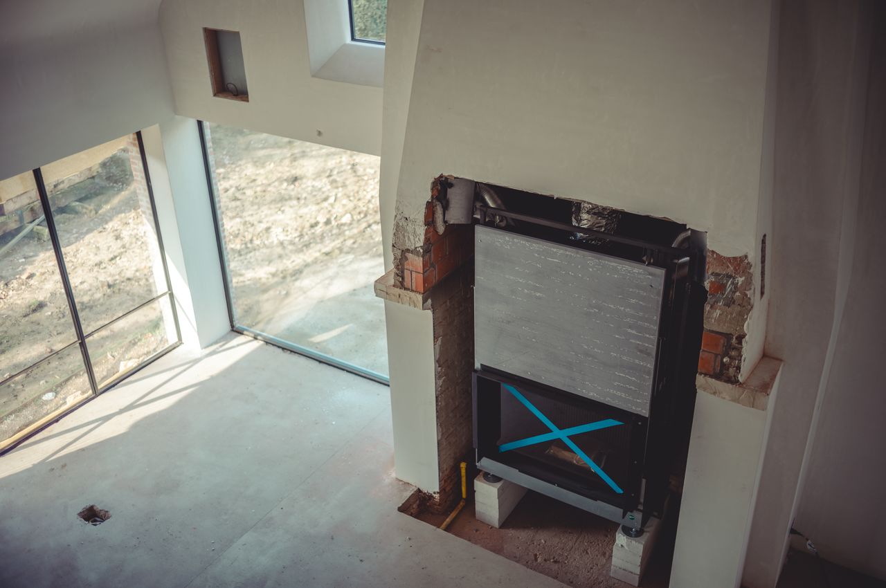 A fireplace insert is standing in large open fireplace. Open space around insert needs closing and plastering.