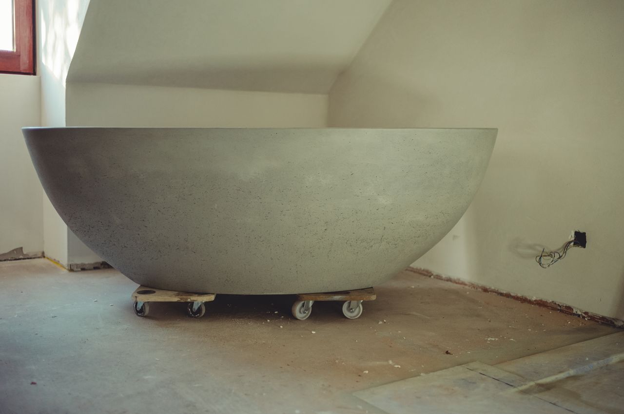 An empty room that is still under construction, that will eventually become a bathroom. The only thing in the room is a concrete tub on temporary wheels.