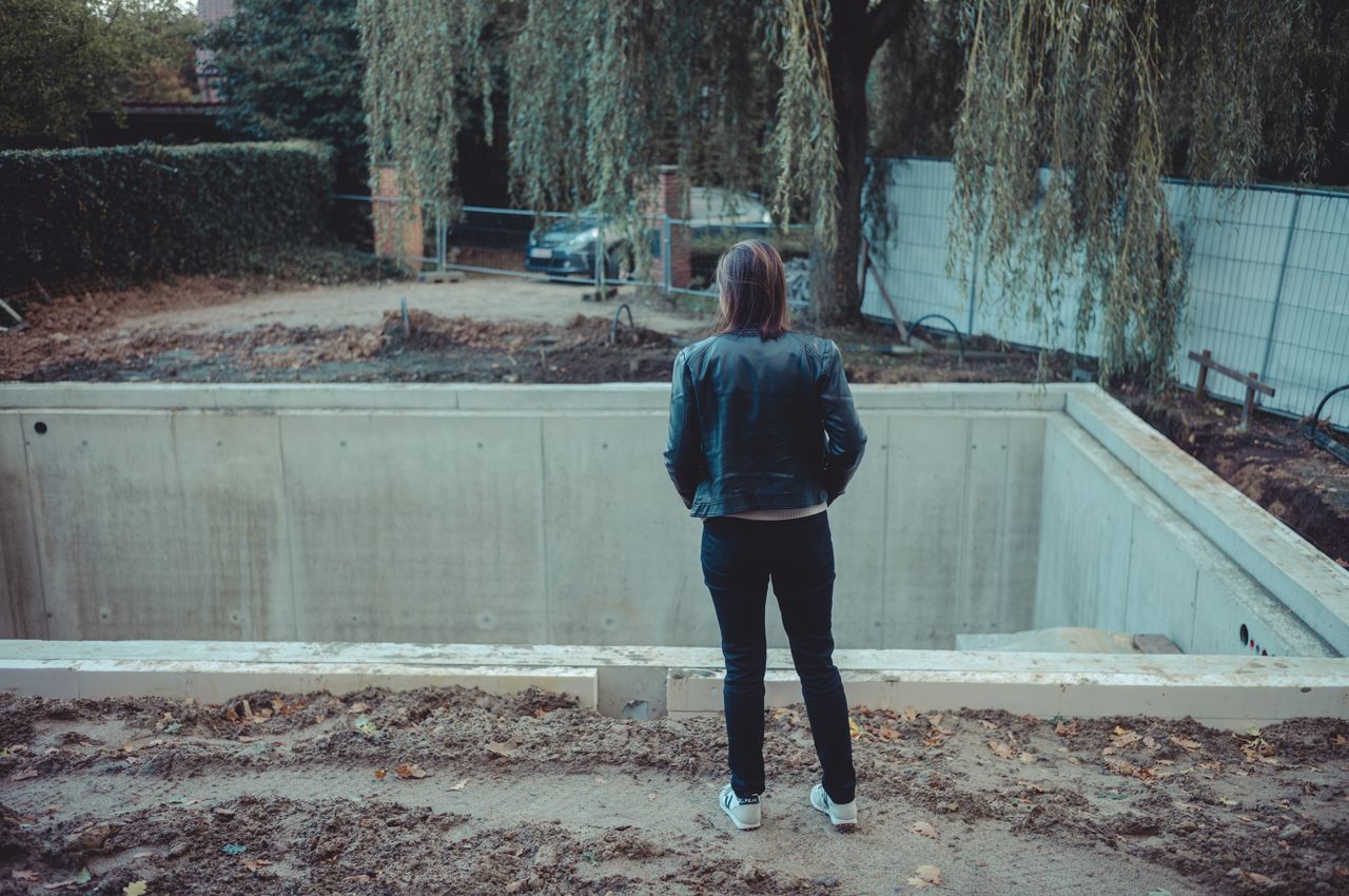 A person in a black jacket stands at the edge of a concrete basement under construction for a future garage.