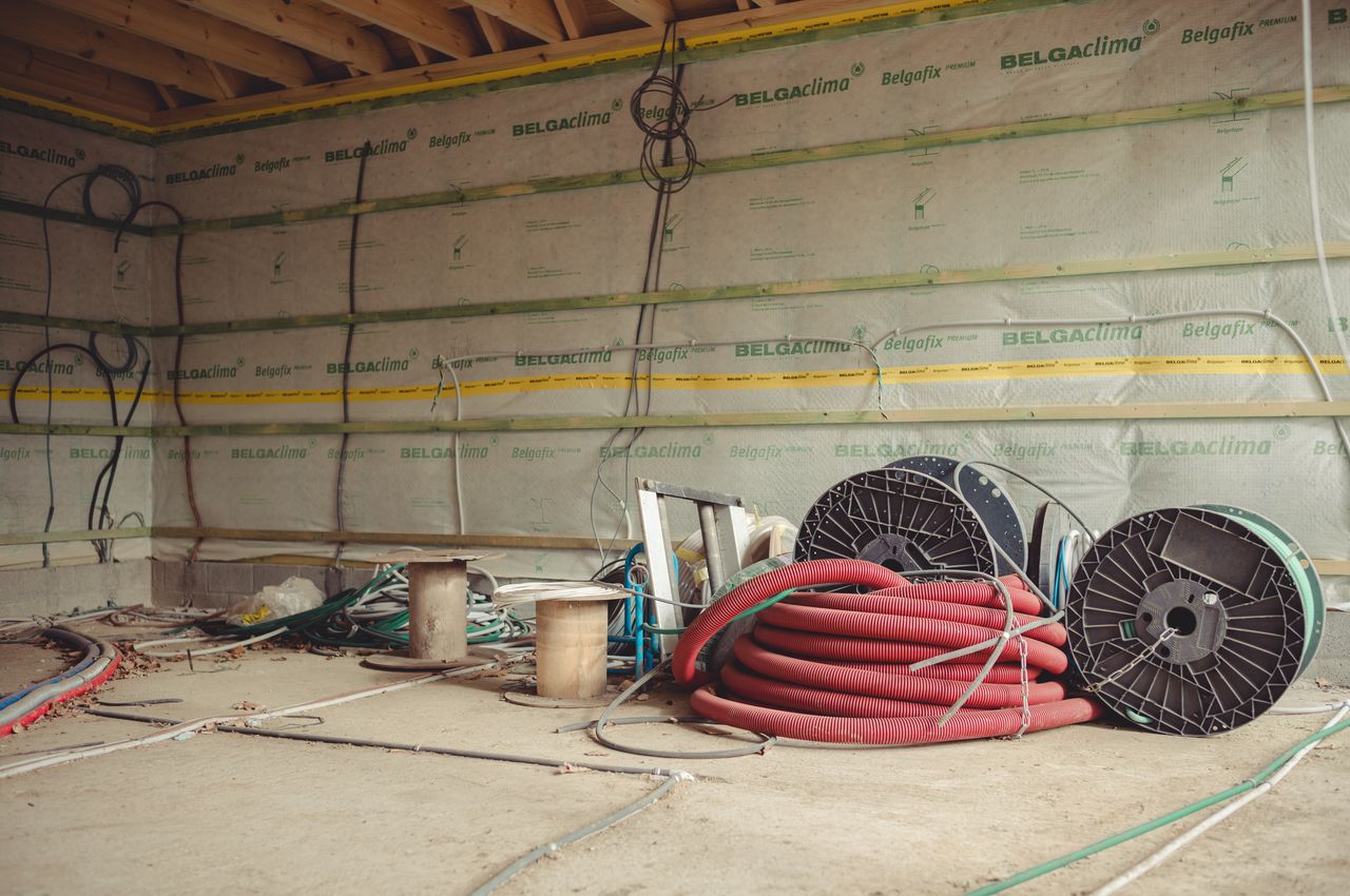 An unfinished interior wall with electrical wire spools and tubes in the foreground.