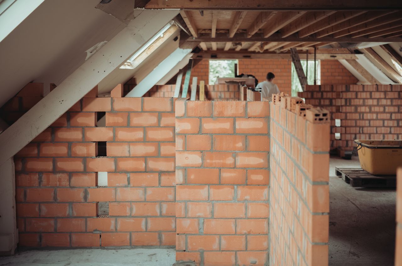Partially built brick walls on the second floor of a barn, with a worker in the background.