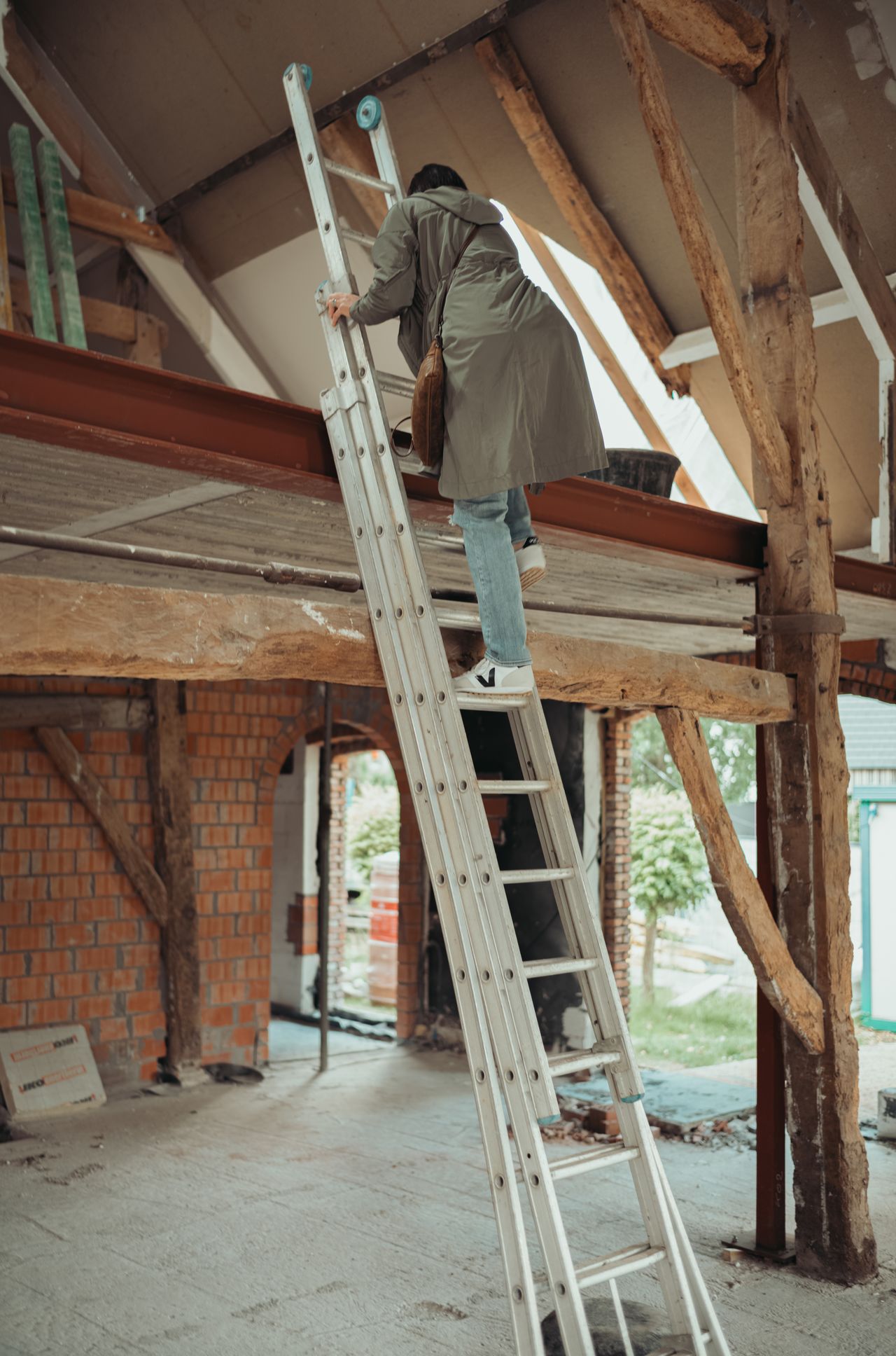 A person climbs a metal ladder to reach the newly completed second floor of a building under construction.