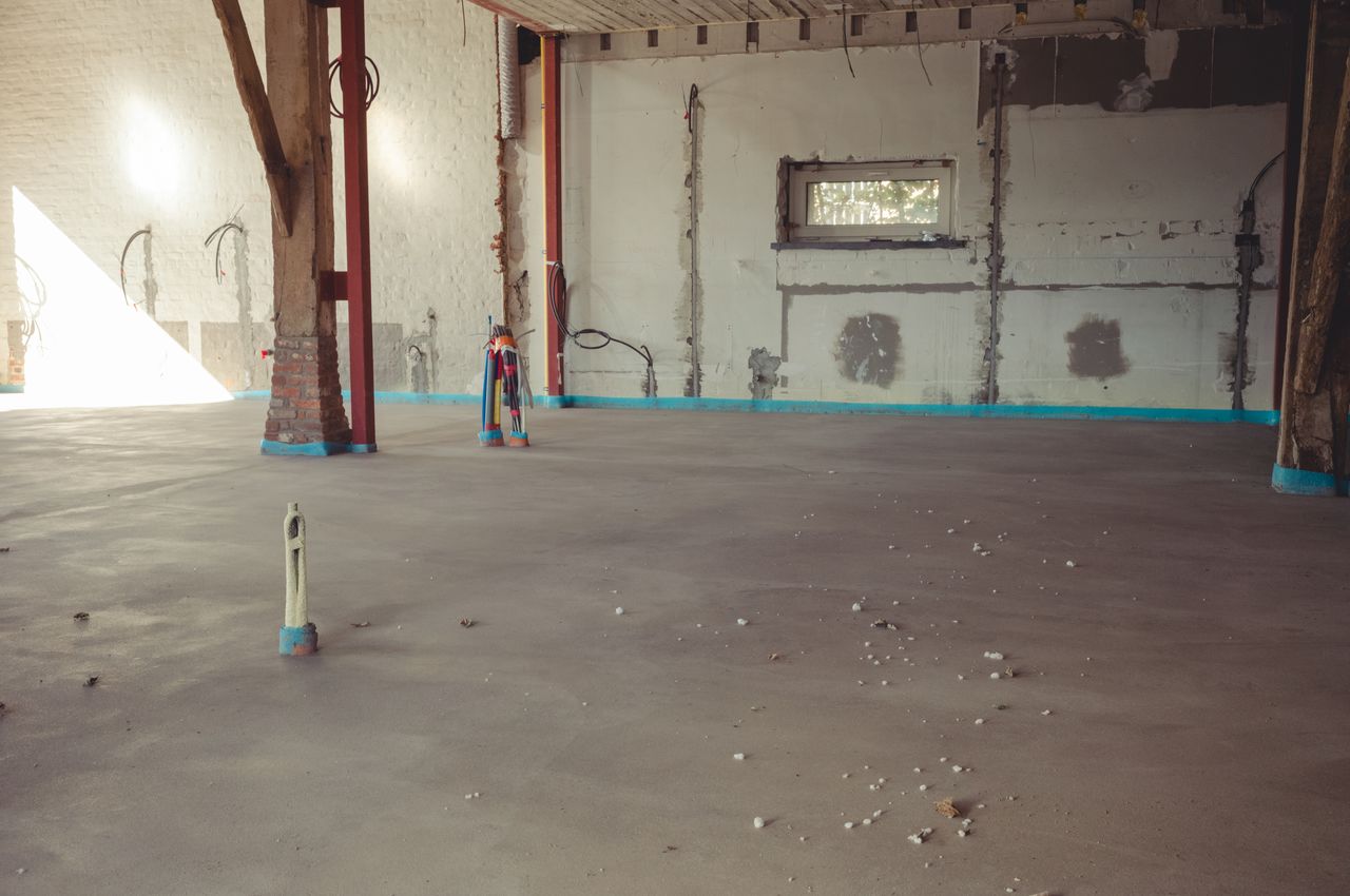 A newly installed subfloor, known as "chape" in Belgium, covers the floor heating system in a renovated space.