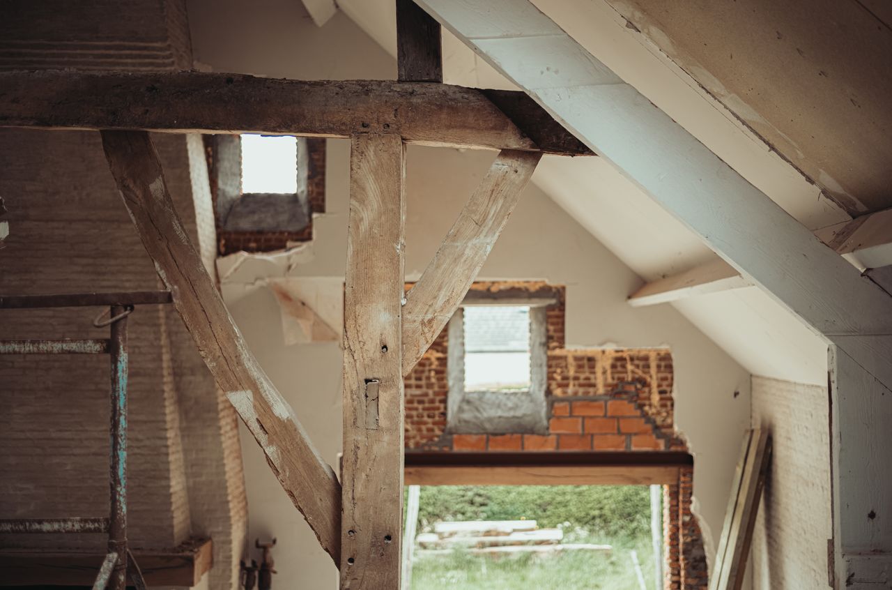 Old wooden beam in the foreground, with newly installed windows in the background letting in natural light.