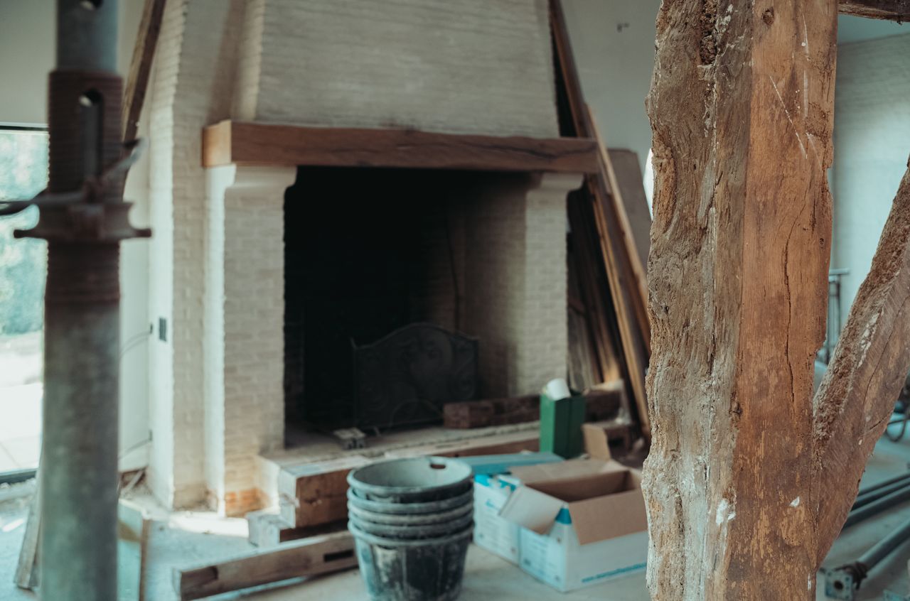 A large brick fireplace in a renovation space with construction materials and tools scattered around.