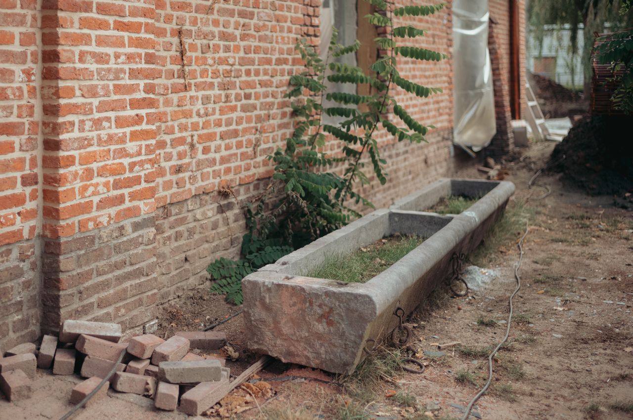 A long, weathered stone trough beside a brick wall, previously used for feeding livestock, now considered for reuse.