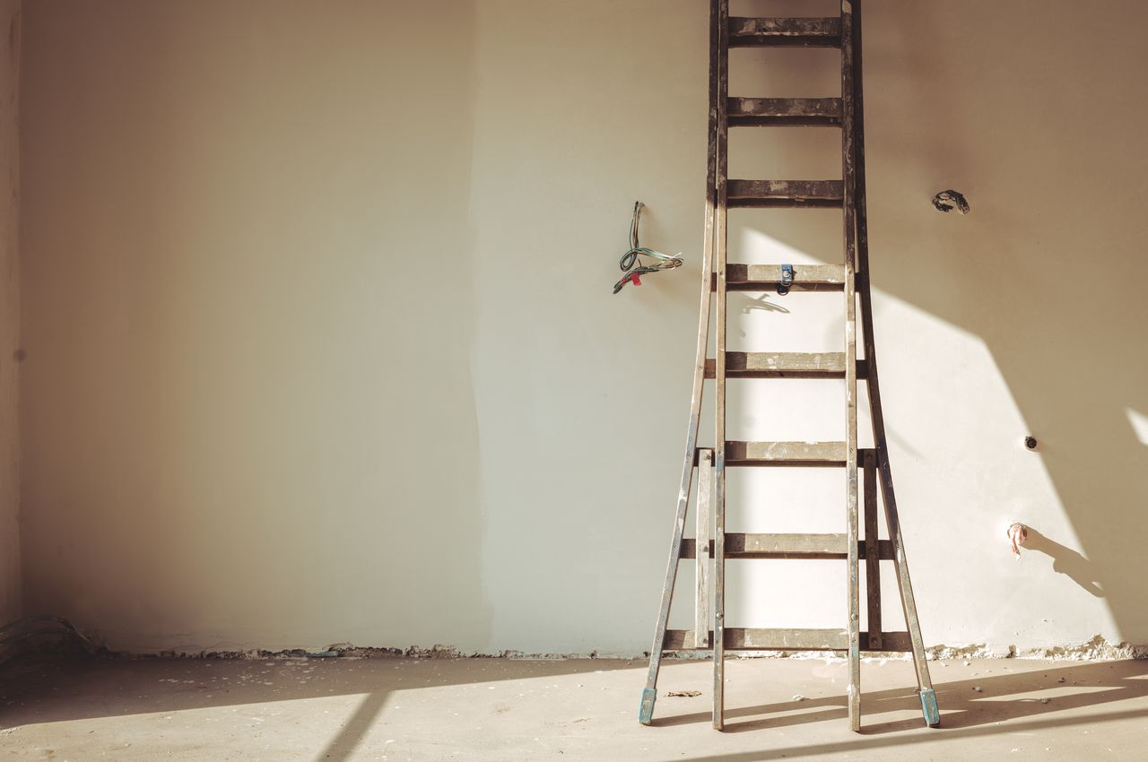 A wall with two paint colors on it and a ladder leaning against it.