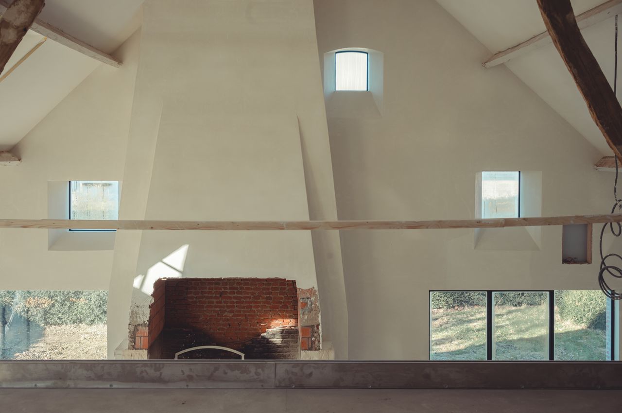 A large two-story interior wall with 3 small windows. The wall is freshly plastered and white. Morning light is beaming through the 3 small windows.