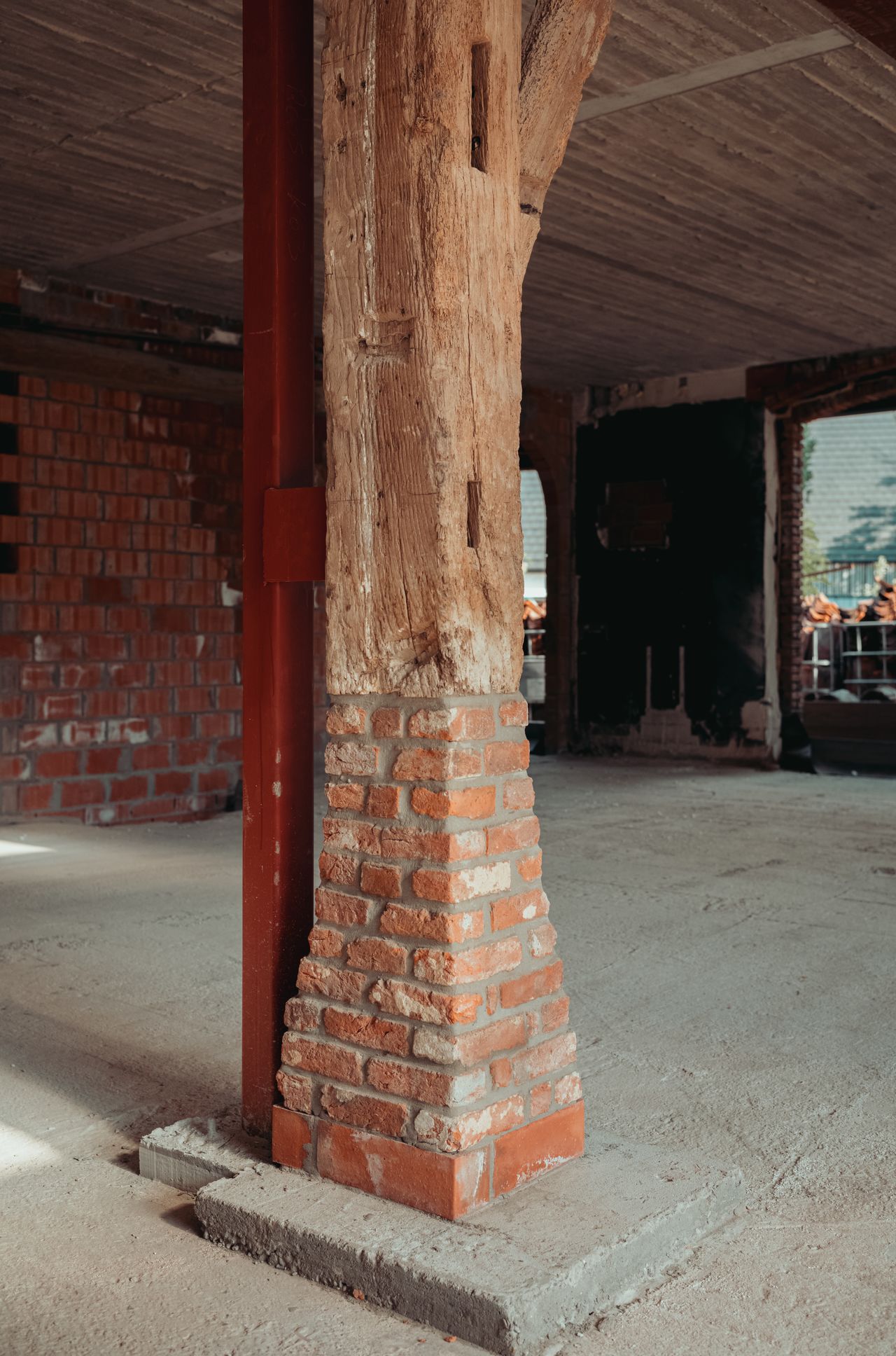 A wooden beam reinforced with a metal support pole and elevated on a brick base inside a renovated building.