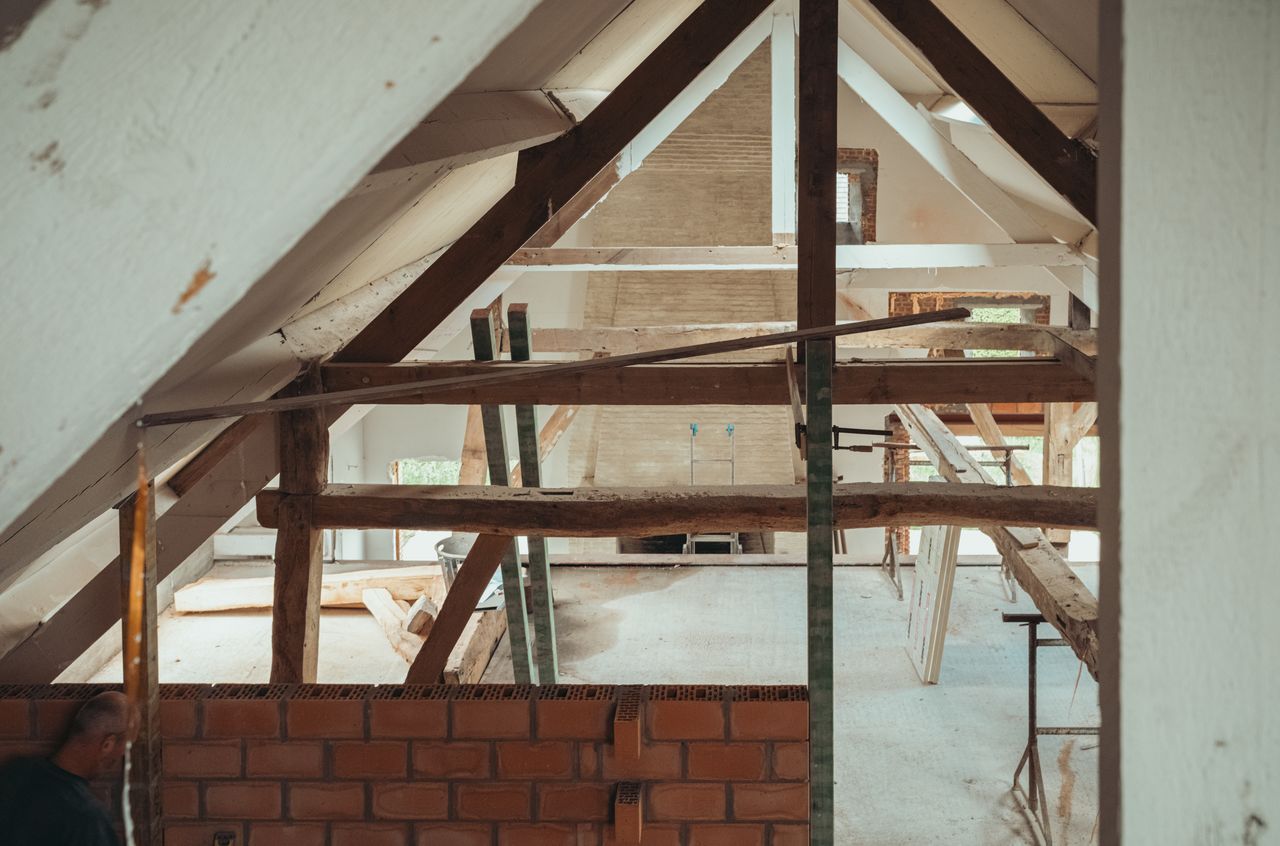 Partially constructed barn roof with exposed wooden beams, brick wall, and construction materials scattered throughout the space.