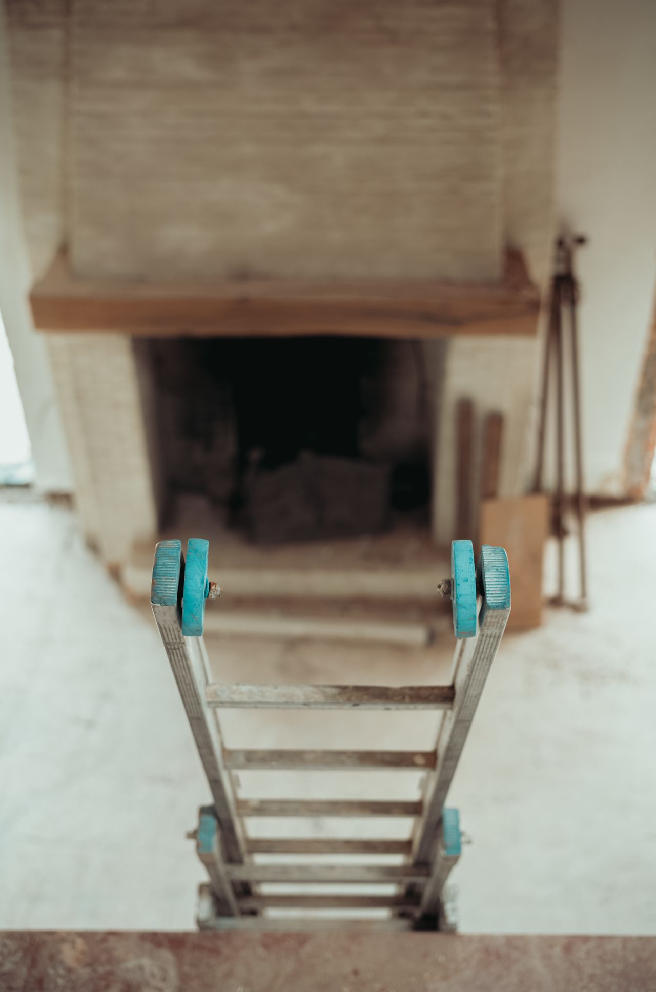 A steep metal ladder with blue handles leads down to the lower floor of a rustic interior space.