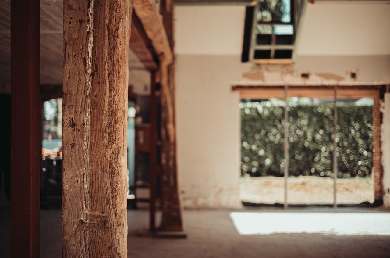 A rough wooden beam in the foreground with a new dormer and enlarged window in the background.