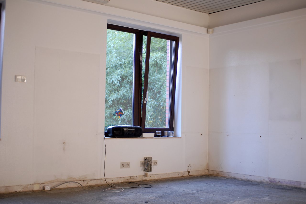 An empty office with a radio and glasses on the windowsill, an open window, and exposed electrical outlets.