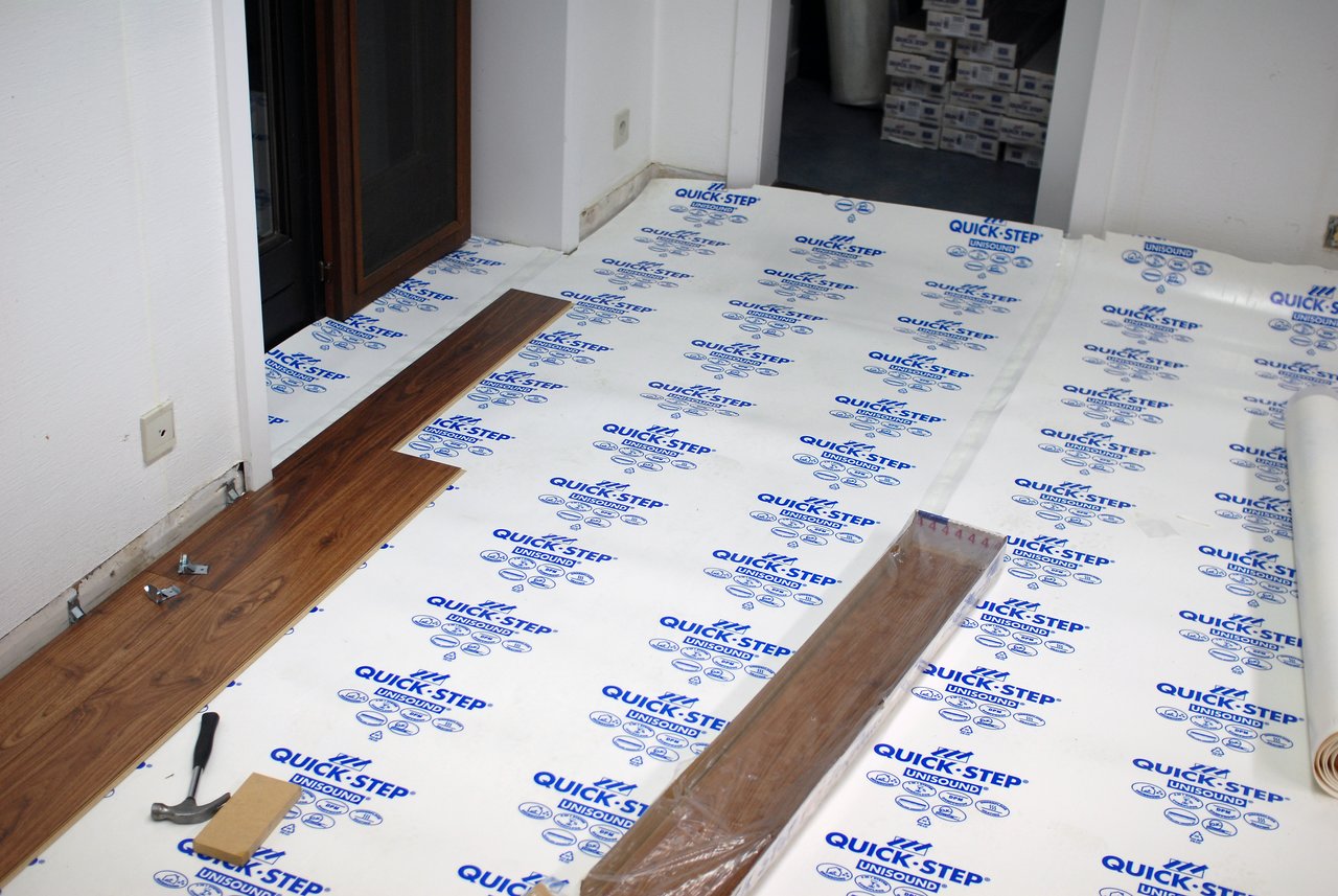 Partially installed wooden flooring in an office, with tools and materials scattered on a protective underlayment.