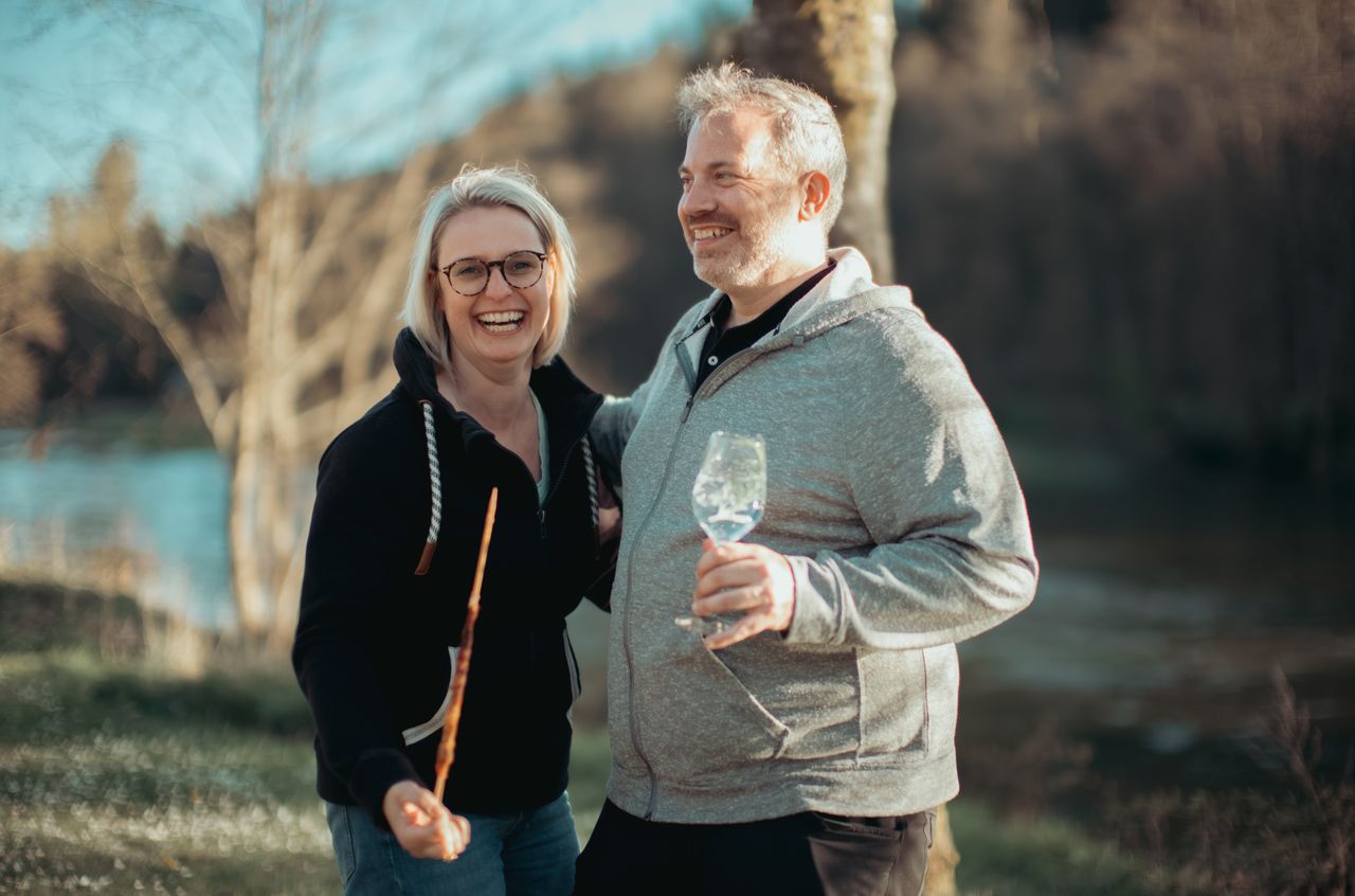 A smiling woman holds a stick while standing next to a man holding a glass outdoors.