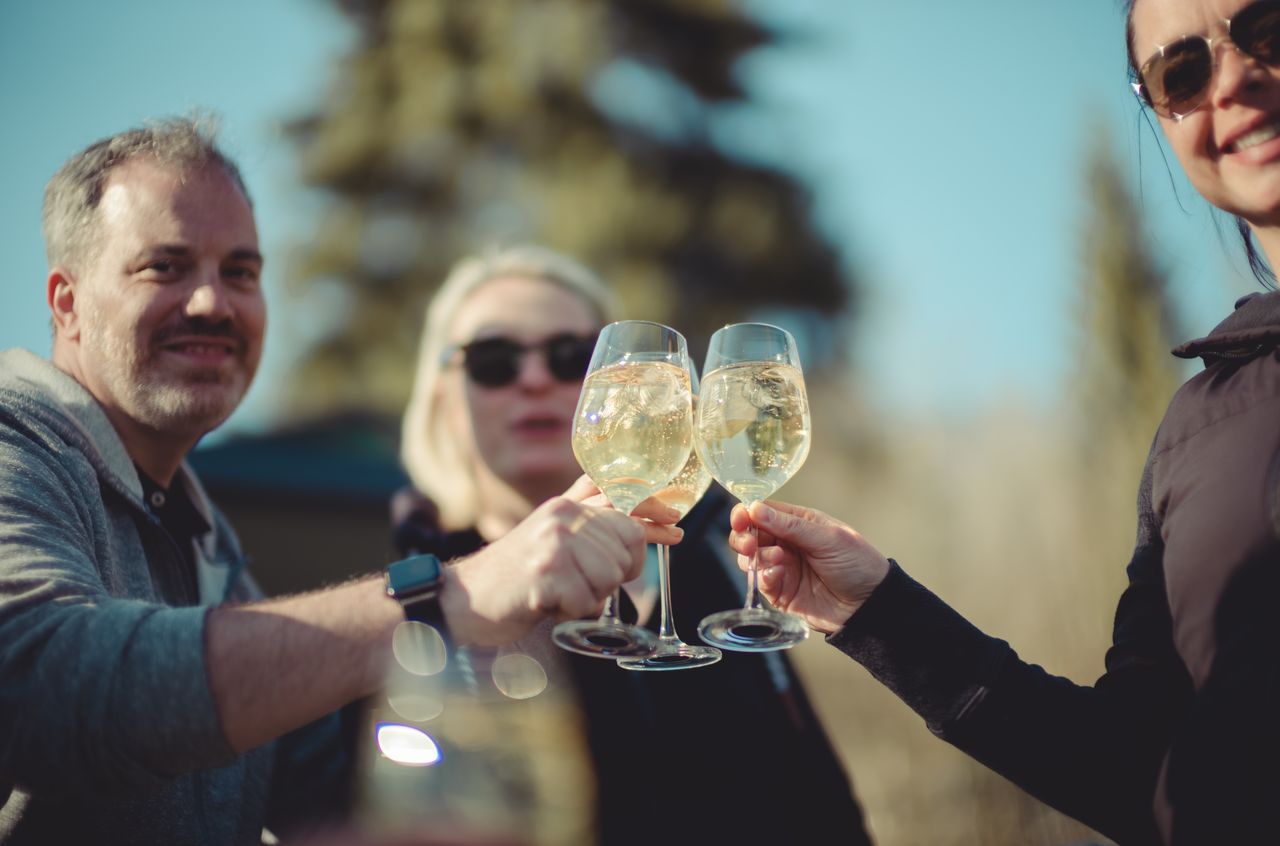 Three people clink glasses of white wine together outdoors, smiling and enjoying a moment.
