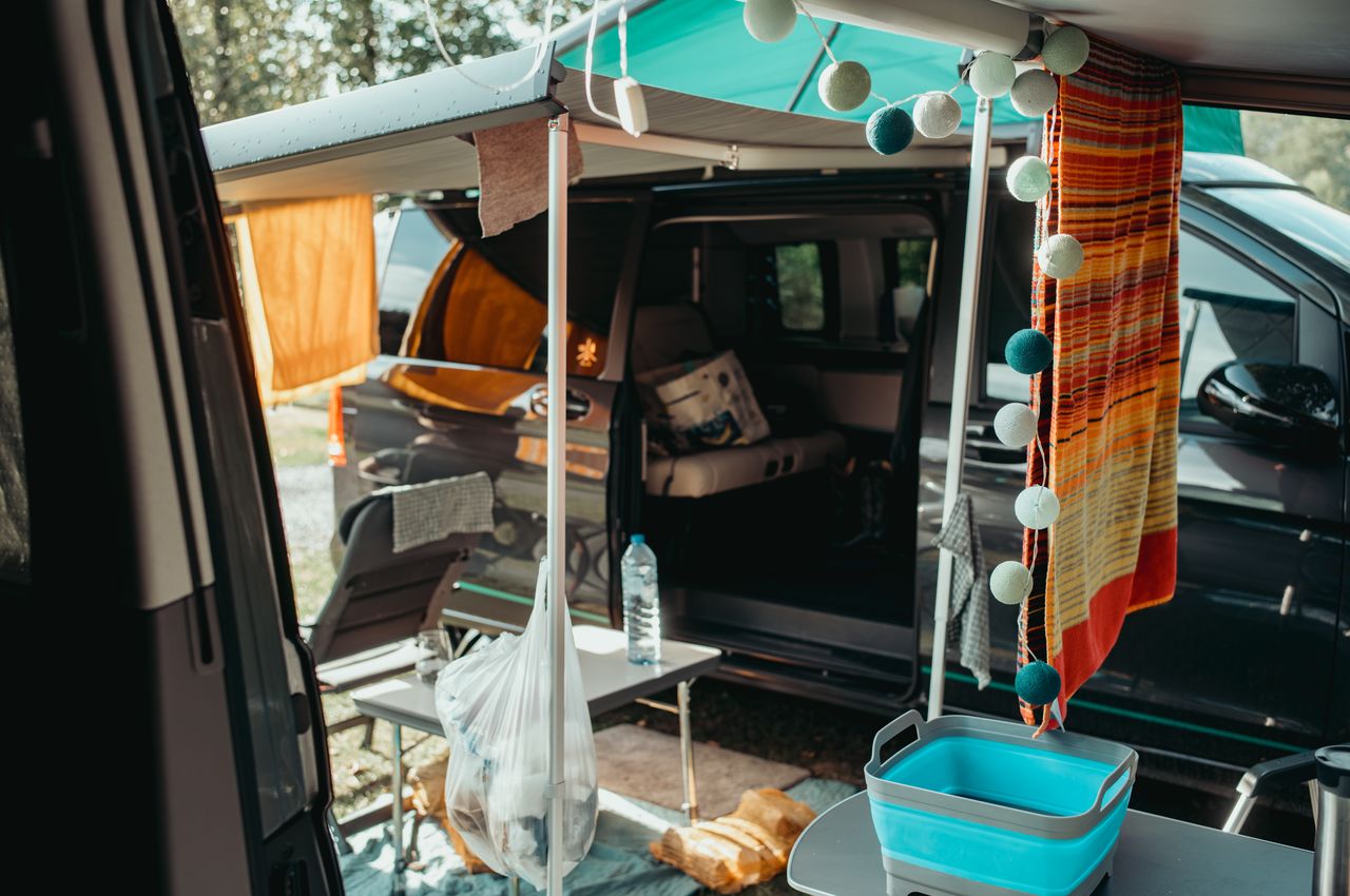 Two vans parked side by side with connected awnings, creating a sheltered outdoor space with chairs and decorations.