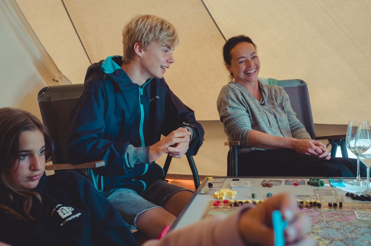 A group of people playing a board game inside a tent, chatting and laughing together.