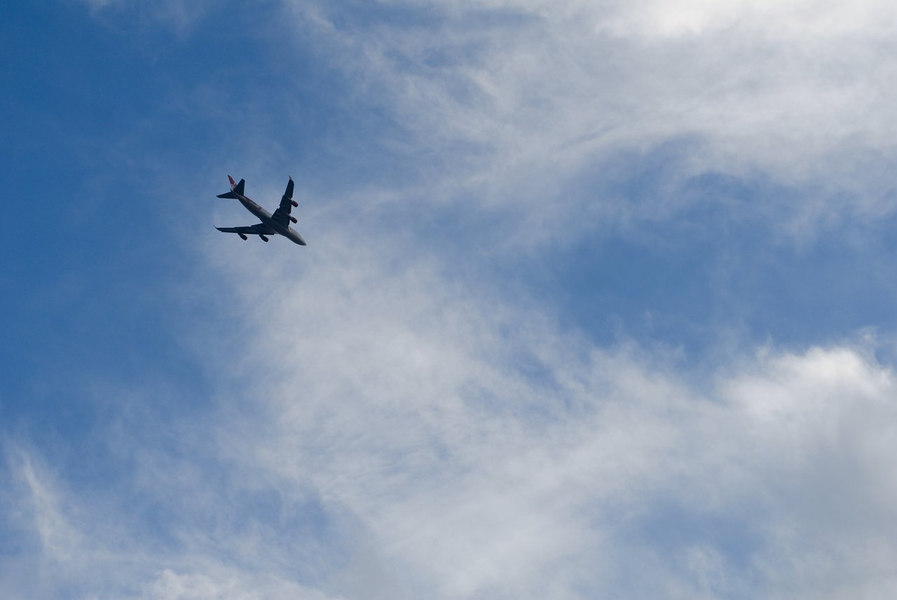 A large airplane flies through the sky with scattered clouds in the background.