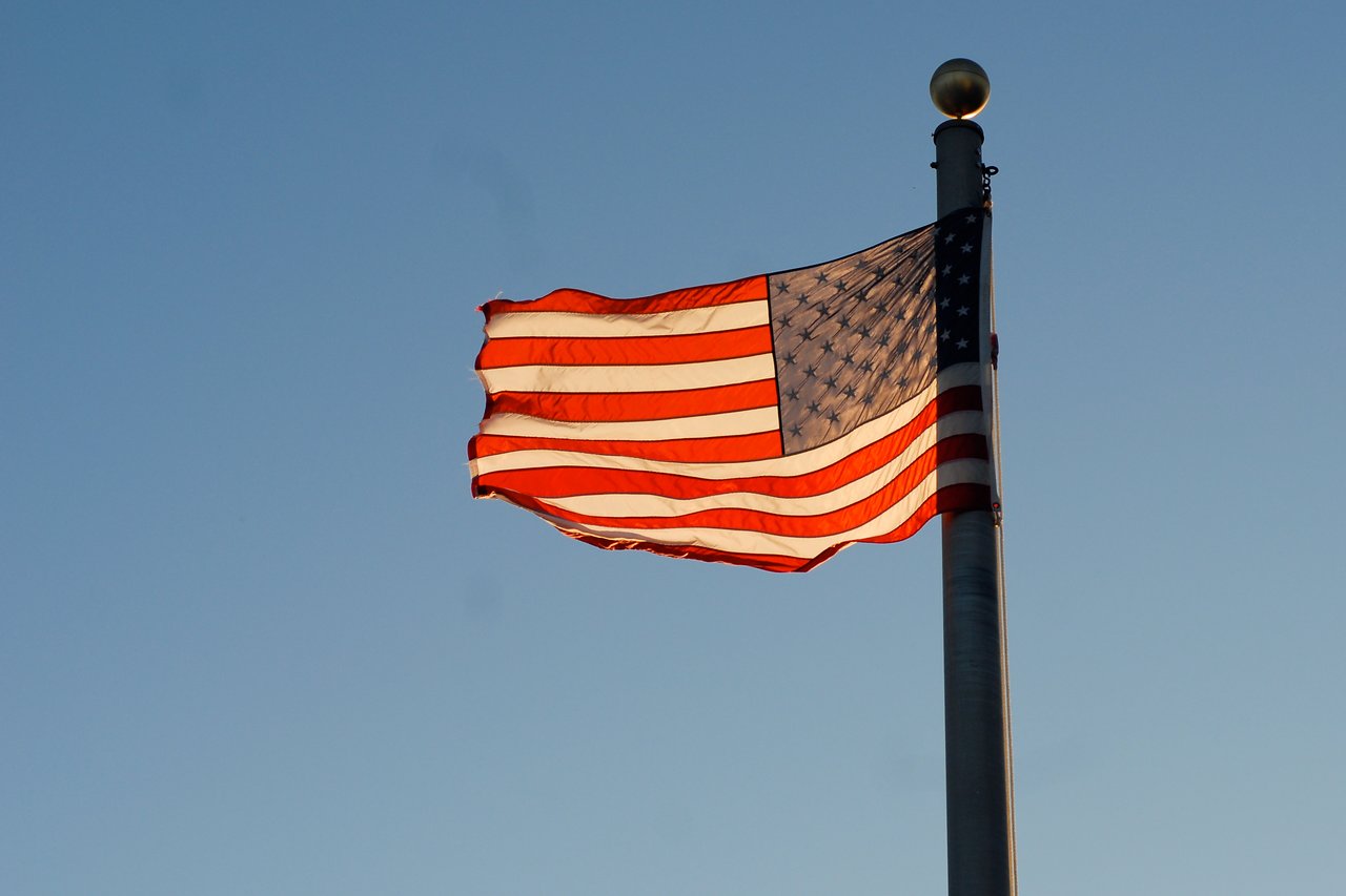 An American flag waves on a flagpole against a clear blue sky.