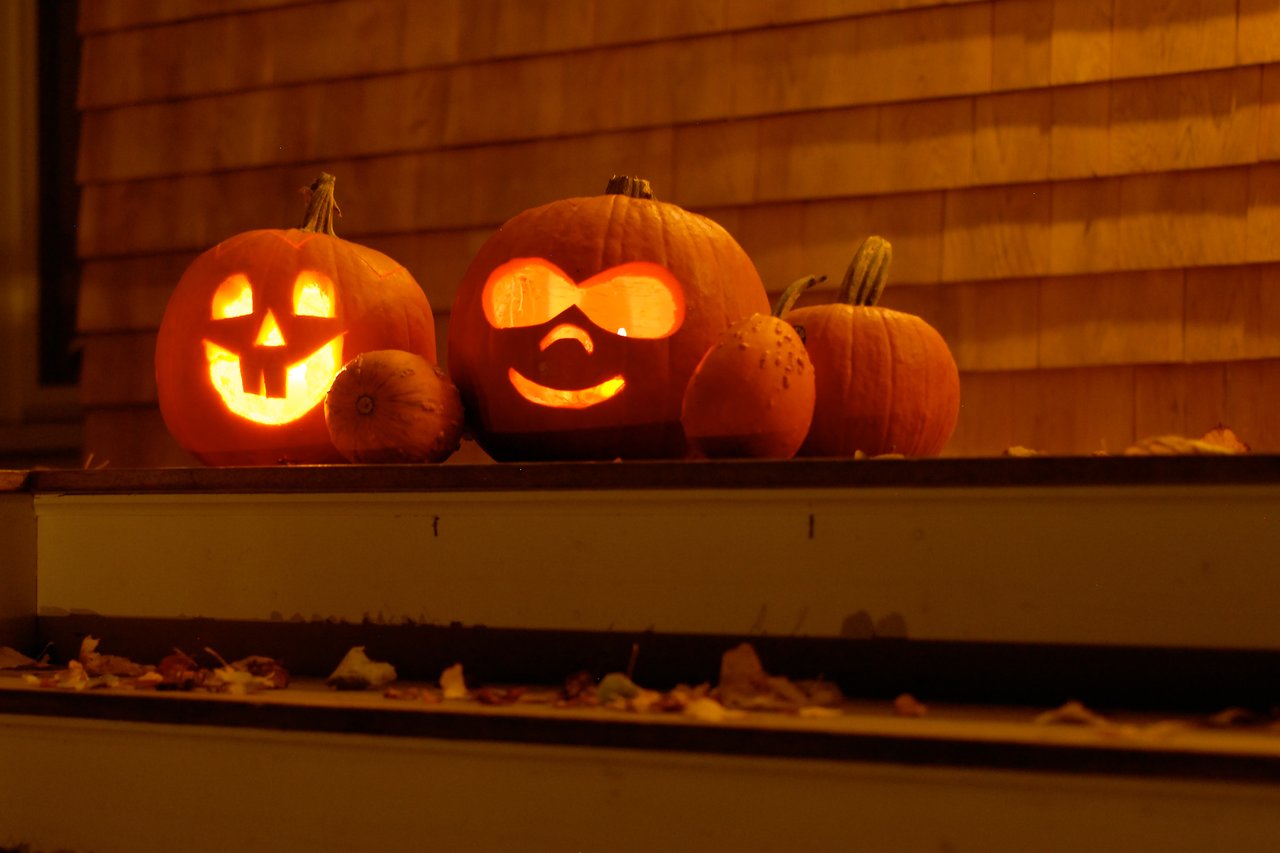Two glowing jack-o'-lanterns on a porch, one carved with the Druplicon logo, surrounded by smaller pumpkins.