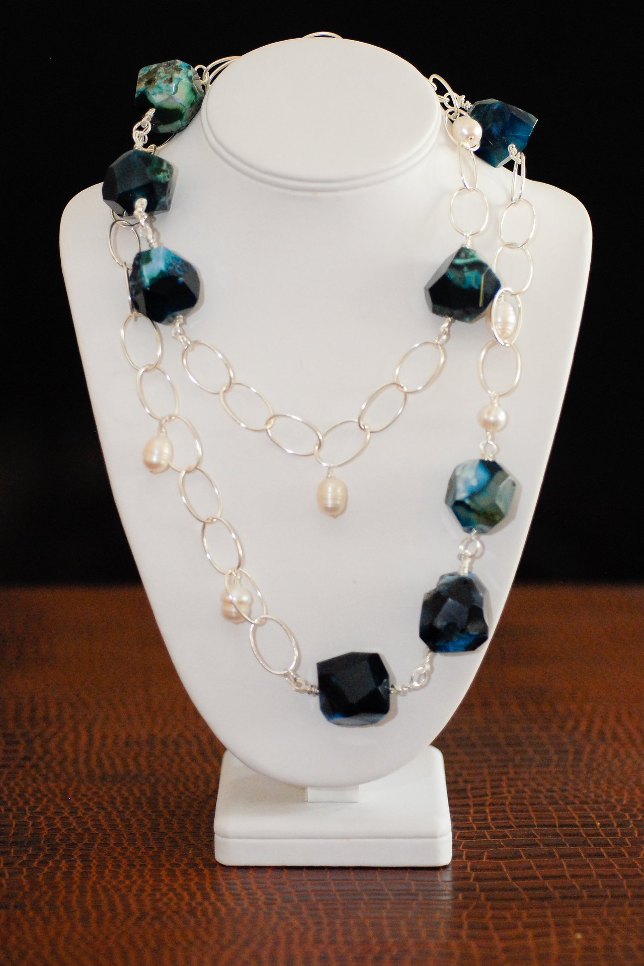 A beaded necklace with blue gemstones and pearls displayed on a white jewelry stand.