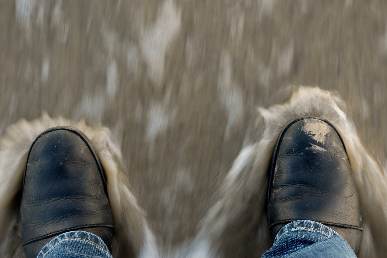Black shoes and blue jeans standing in moving water, creating small splashes around the feet.