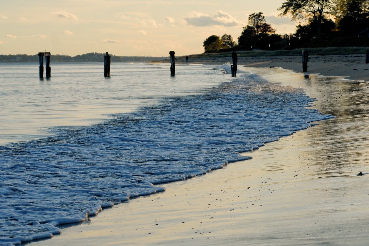 Waves gently wash onto the sandy shore at West Beach, with wooden pilings standing in the water.