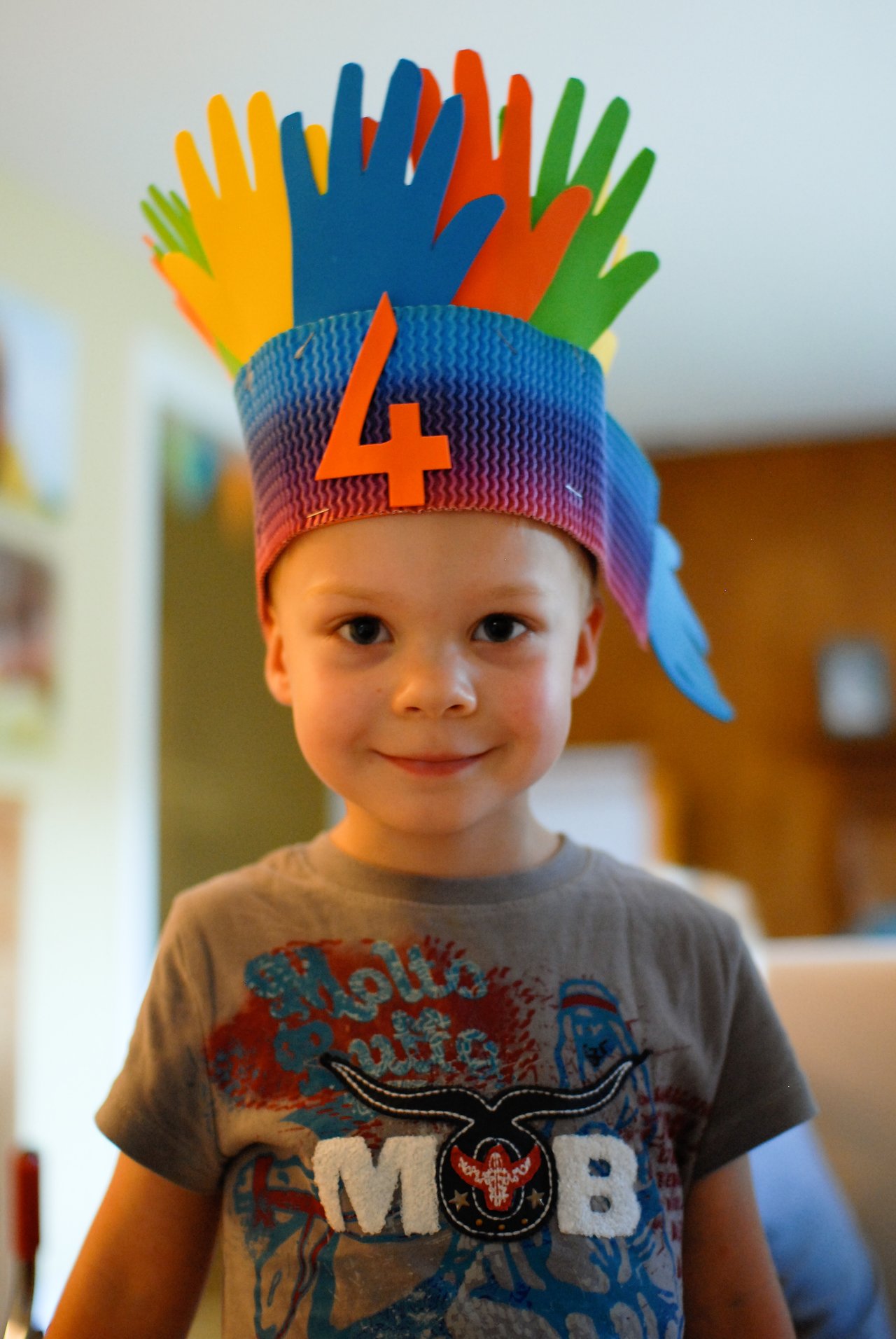 A young child wearing a colorful handmade crown with a number four, smiling at the camera.
