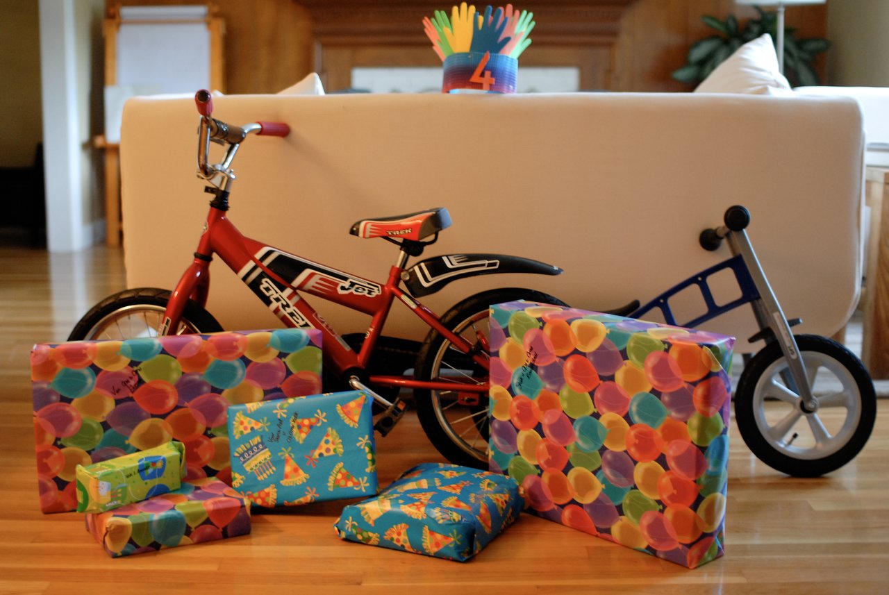A red bicycle, a balance bike, and several wrapped birthday gifts are arranged on a wooden floor.