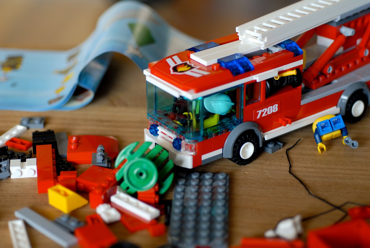 A partially built LEGO fire truck with scattered pieces and an instruction booklet on a wooden surface.