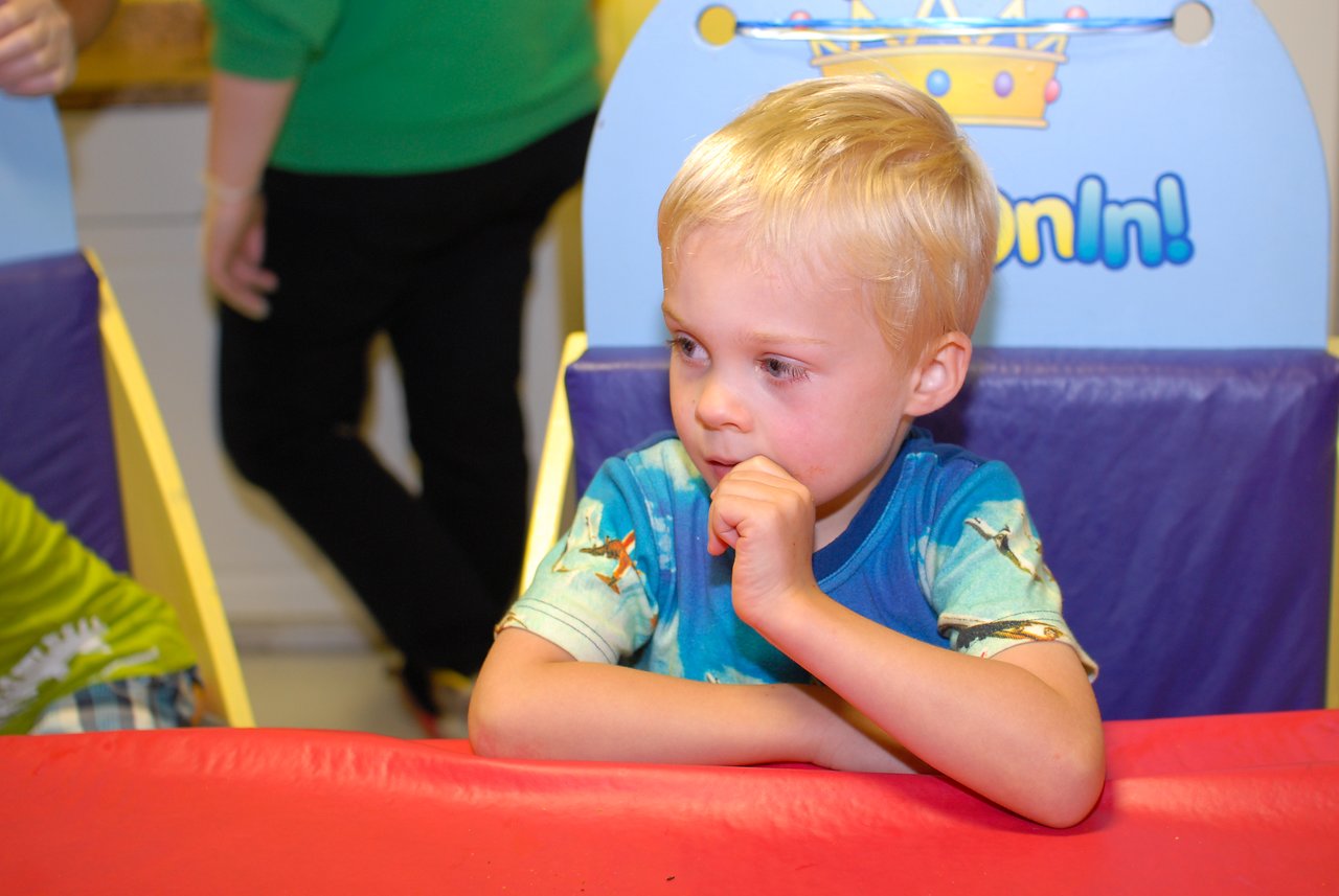 A young child sits at a table, resting his chin on his hand, waiting for birthday cake.