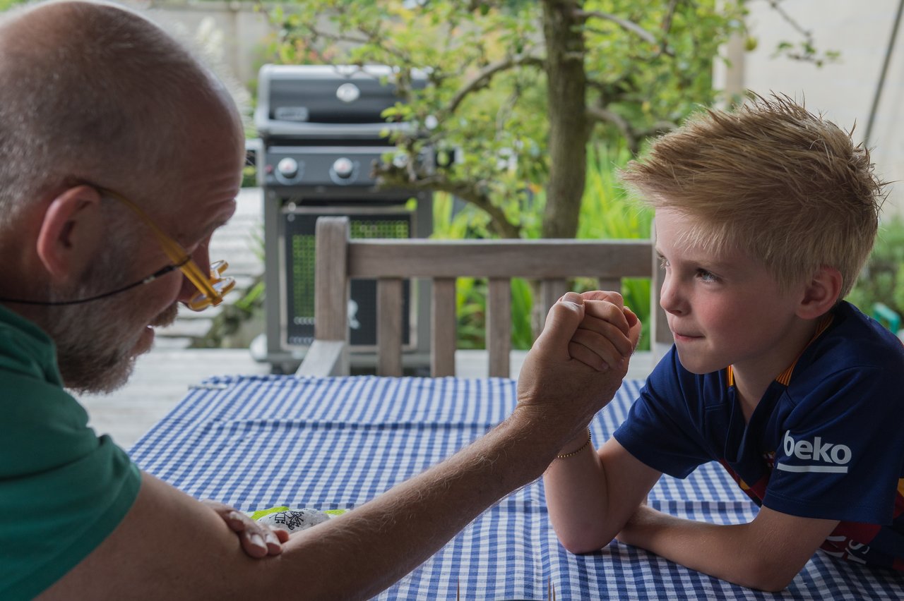 A man and a boy arm wrestle at a table, both focused and determined.